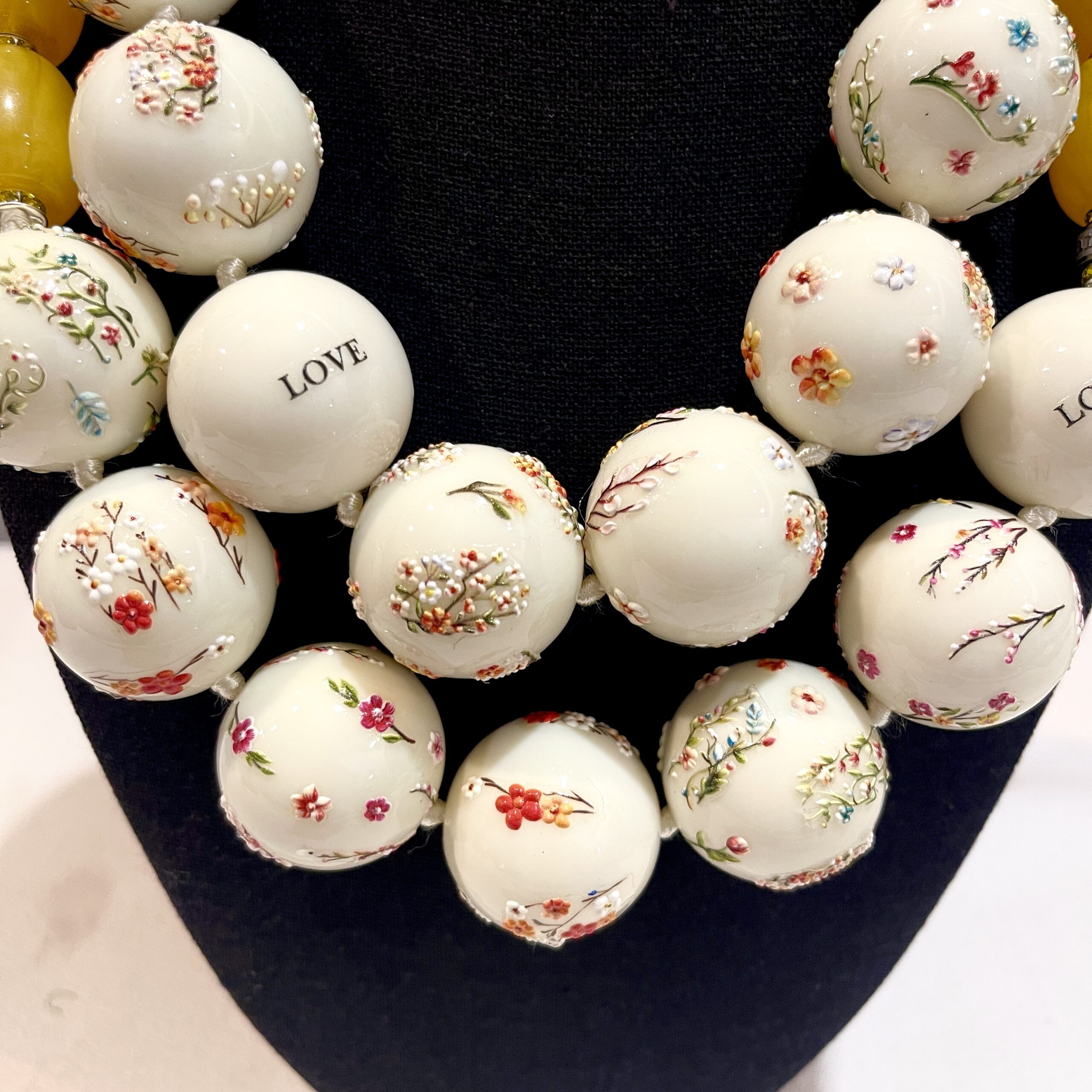 Two‑strand acrylic bead necklace set with floral designs and beeswax‑diluted yellow beads displayed on a black mannequin.