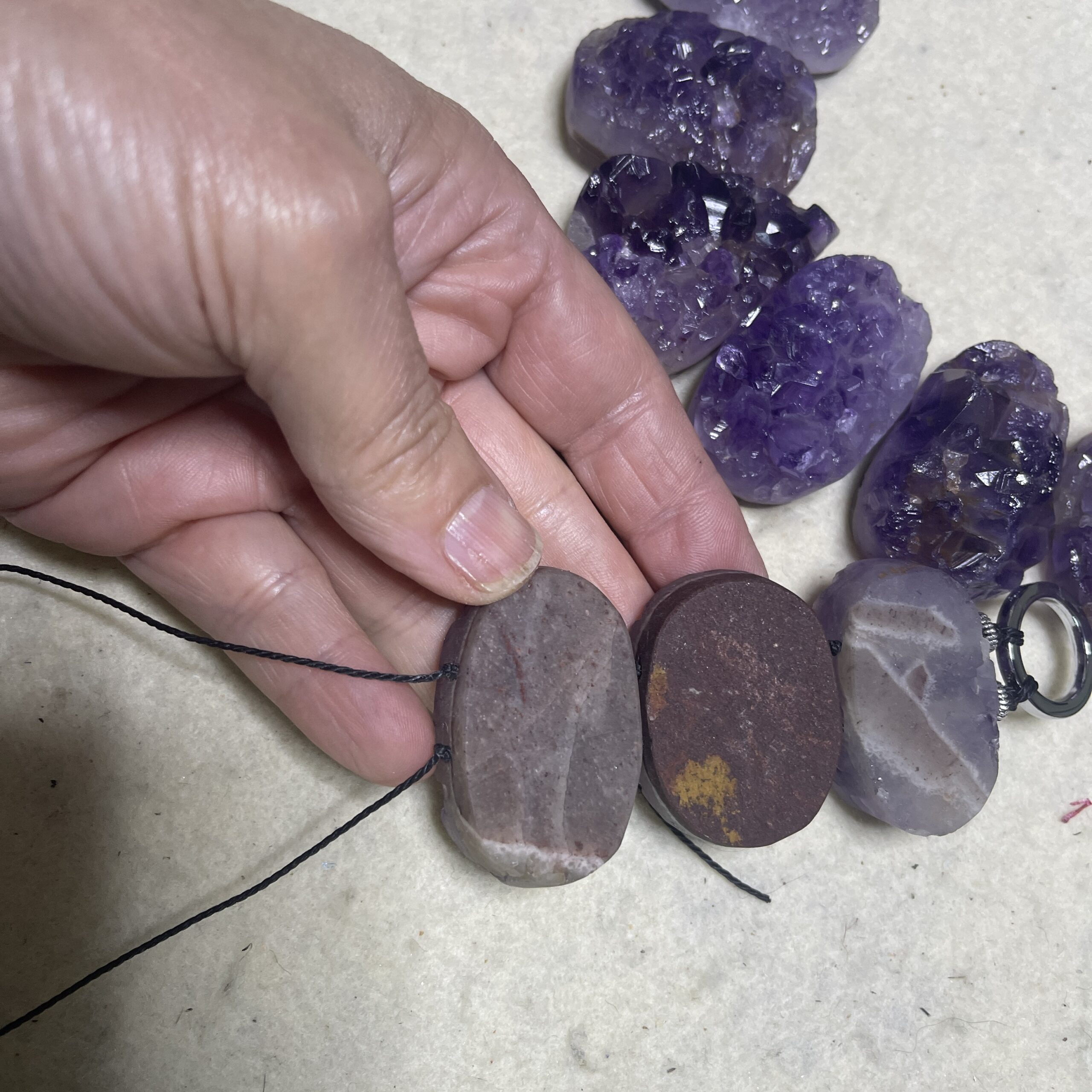 Raw amethyst crystal necklace with brass clasp, featuring natural violet crystal formations displayed on a black background.