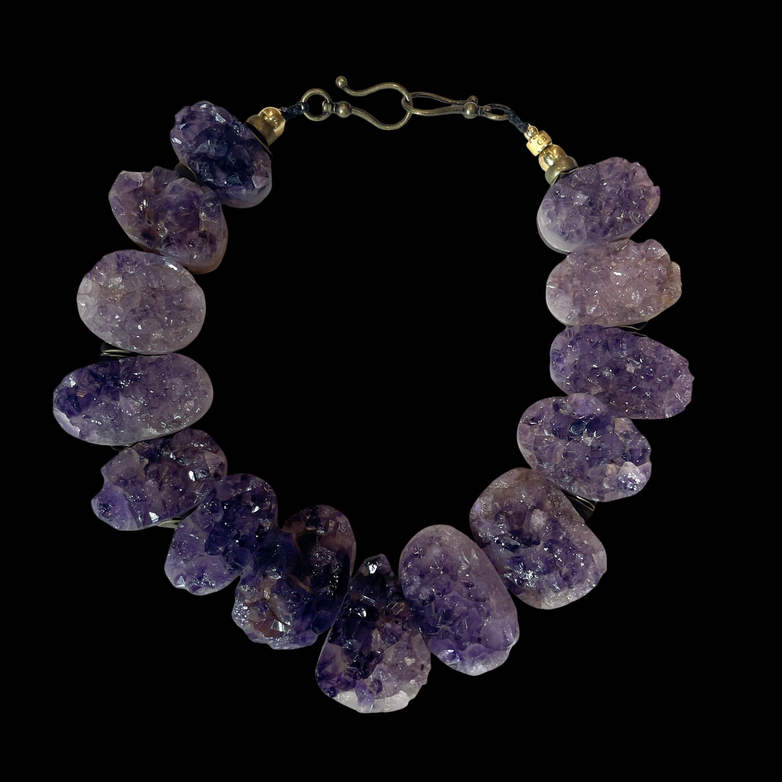 Raw amethyst crystal necklace with brass clasp, featuring natural violet crystal formations displayed on a black background.