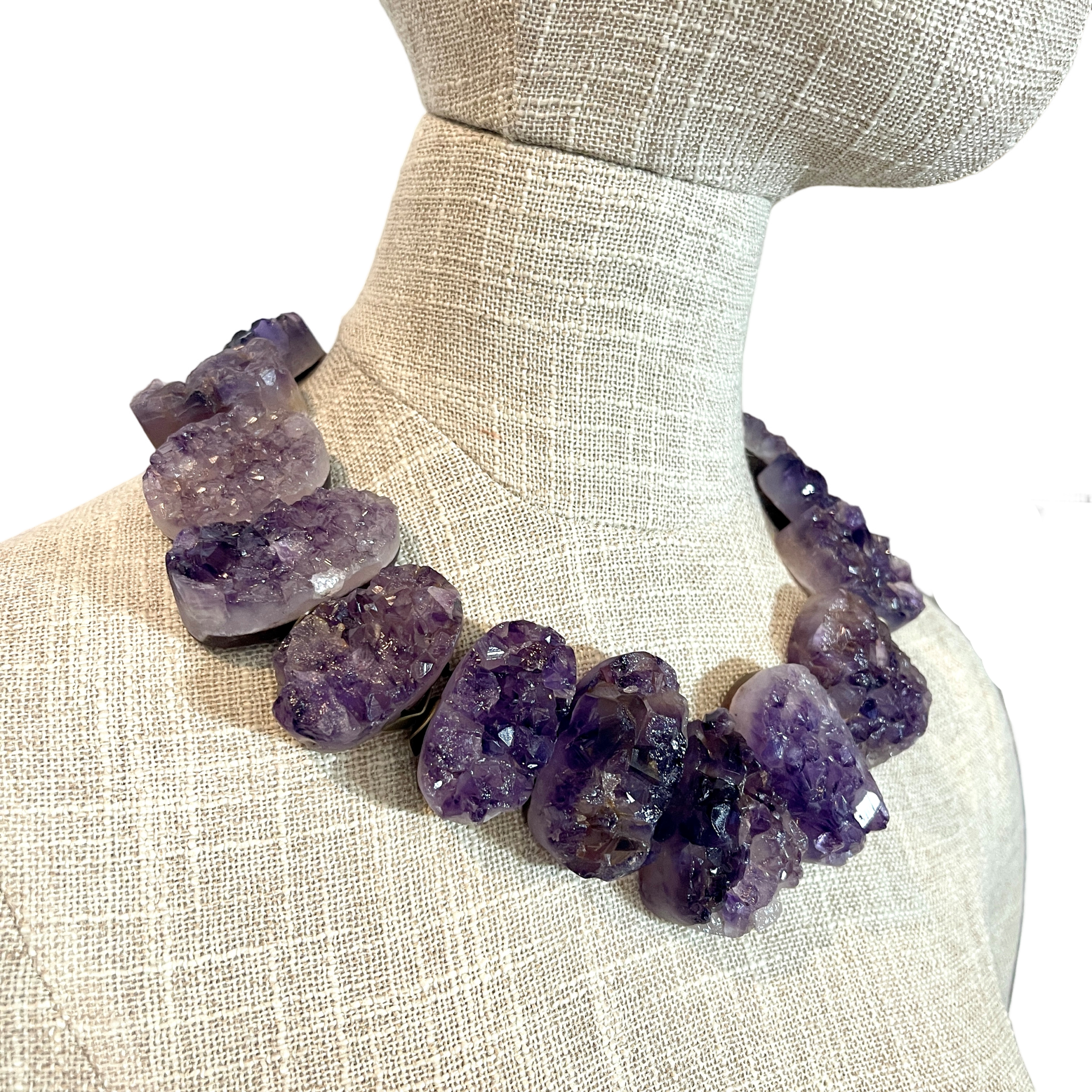 Raw amethyst crystal necklace with brass clasp, featuring natural violet crystal formations displayed on a black background.