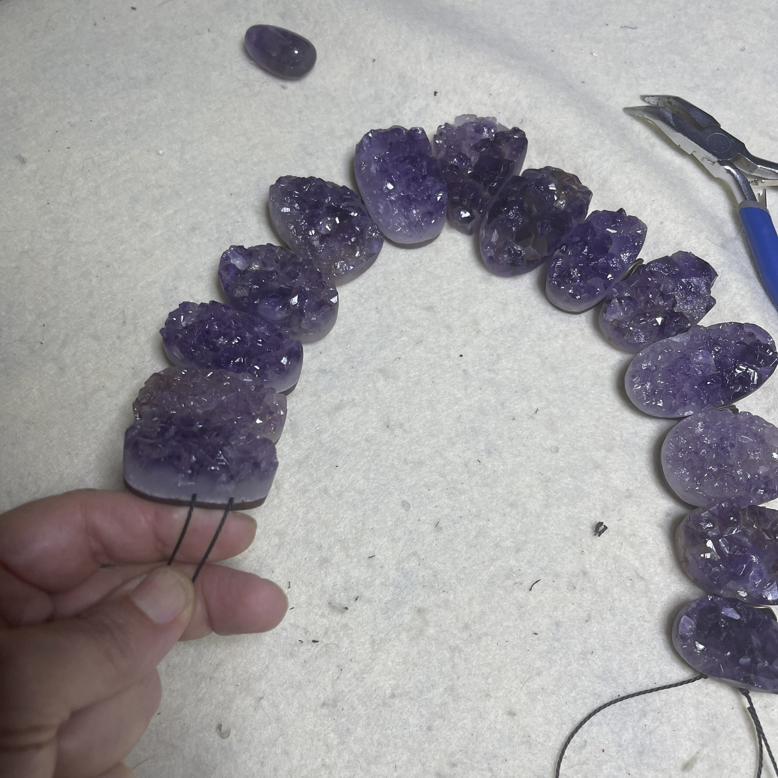 Raw amethyst crystal necklace with brass clasp, featuring natural violet crystal formations displayed on a black background.