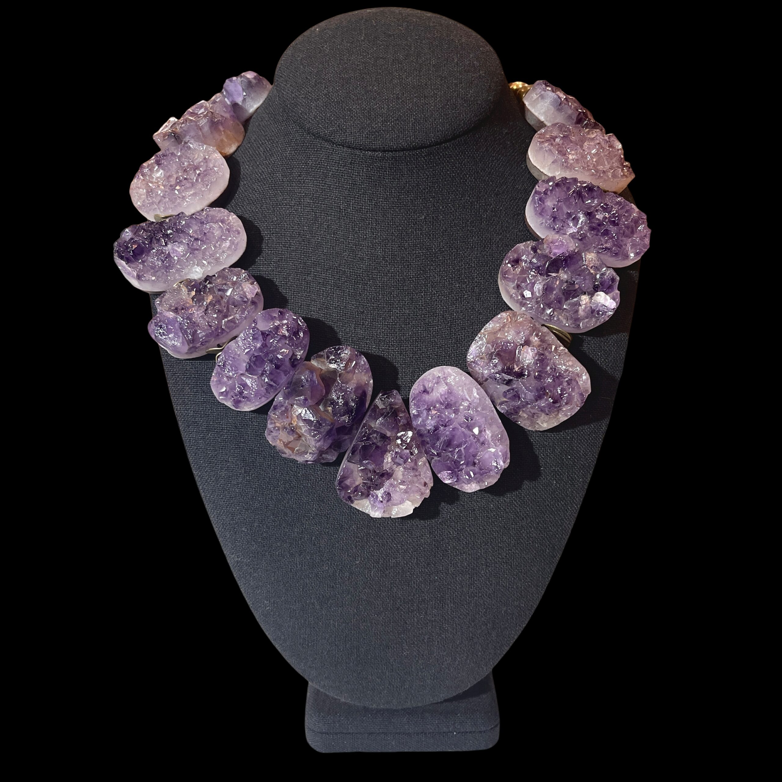 Raw amethyst crystal necklace with brass clasp, featuring natural violet crystal formations displayed on a black background.