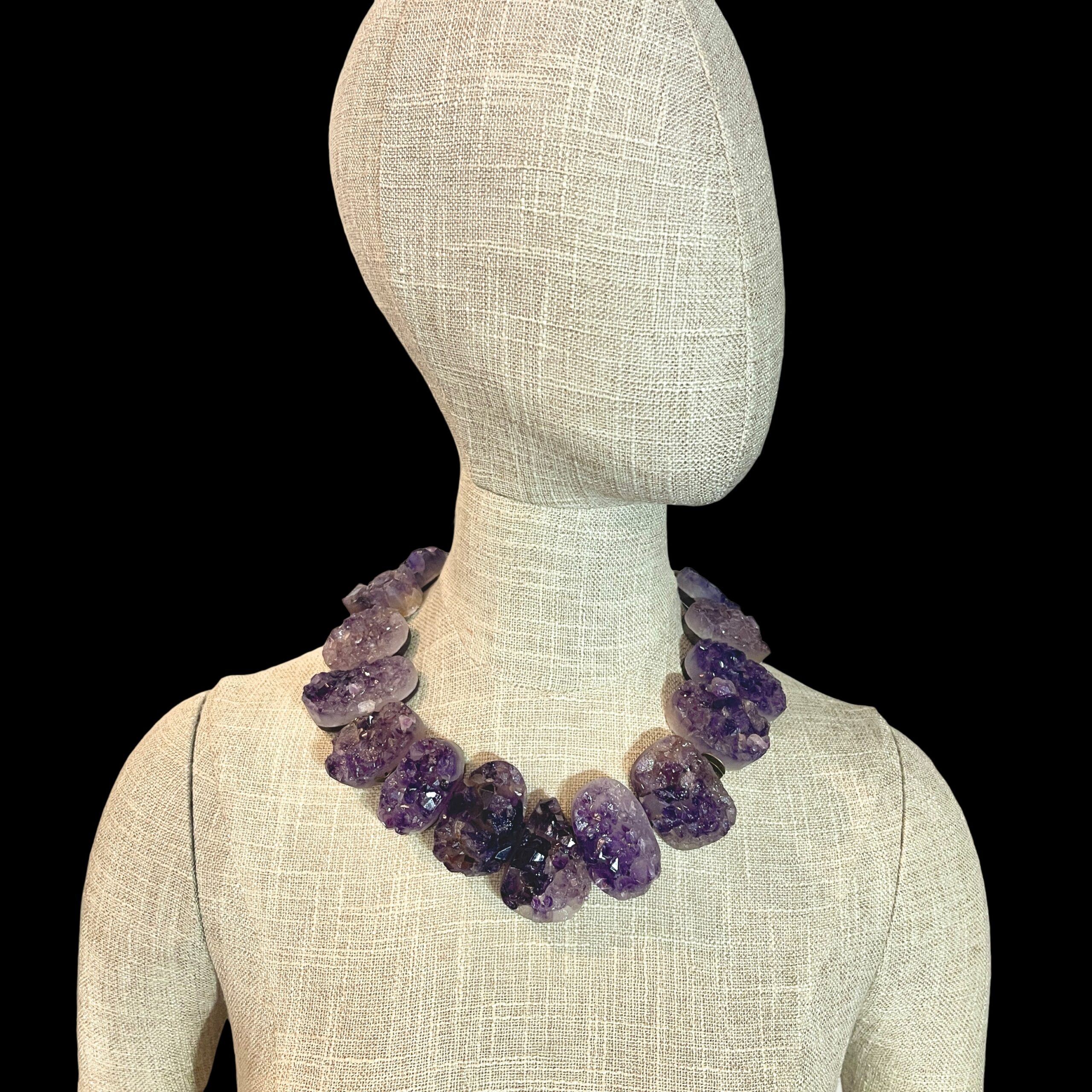 Raw amethyst crystal necklace with brass clasp, featuring natural violet crystal formations displayed on a black background.