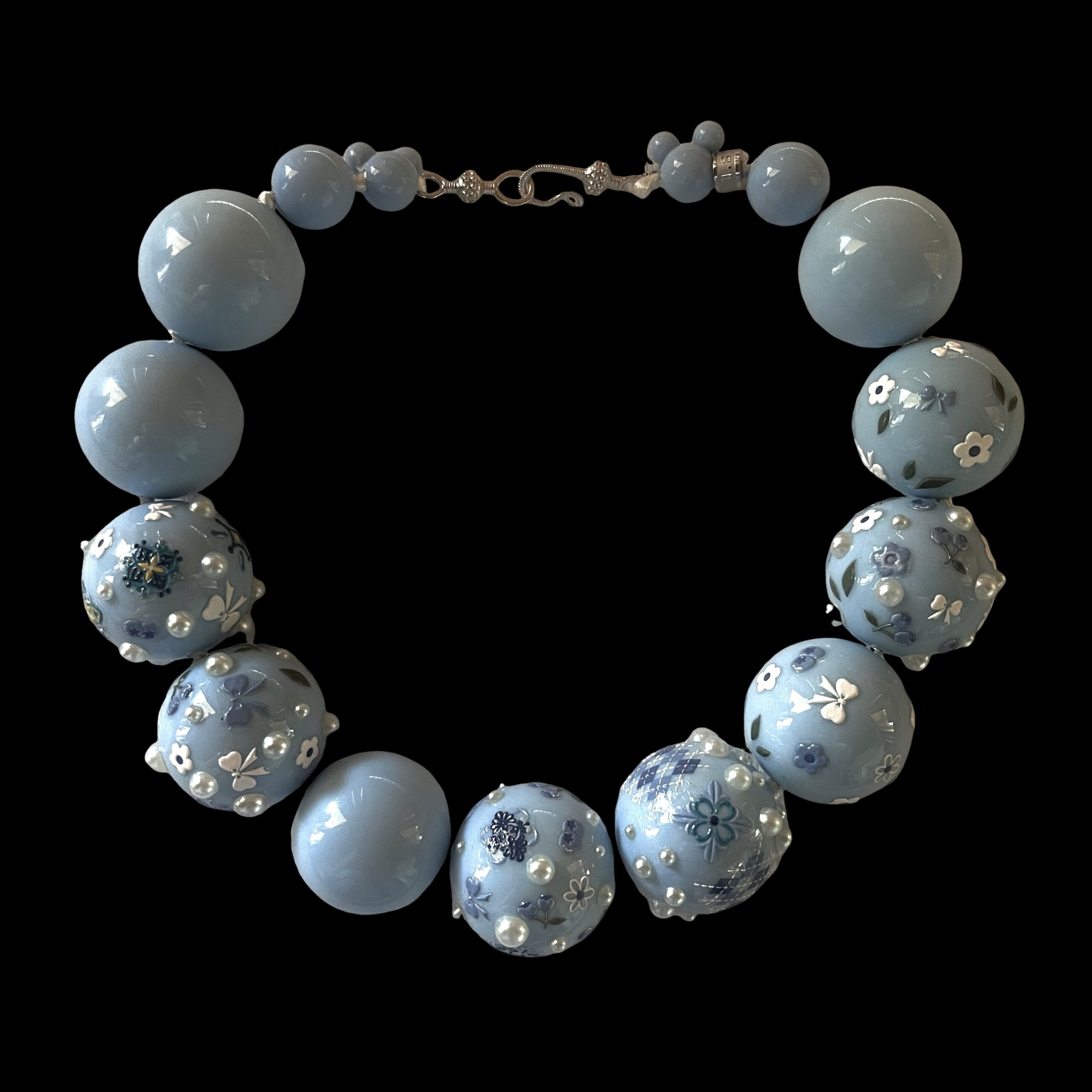 Baby‑blue acrylic bead necklace with floral and bow decorations displayed on a black jewelry bust.