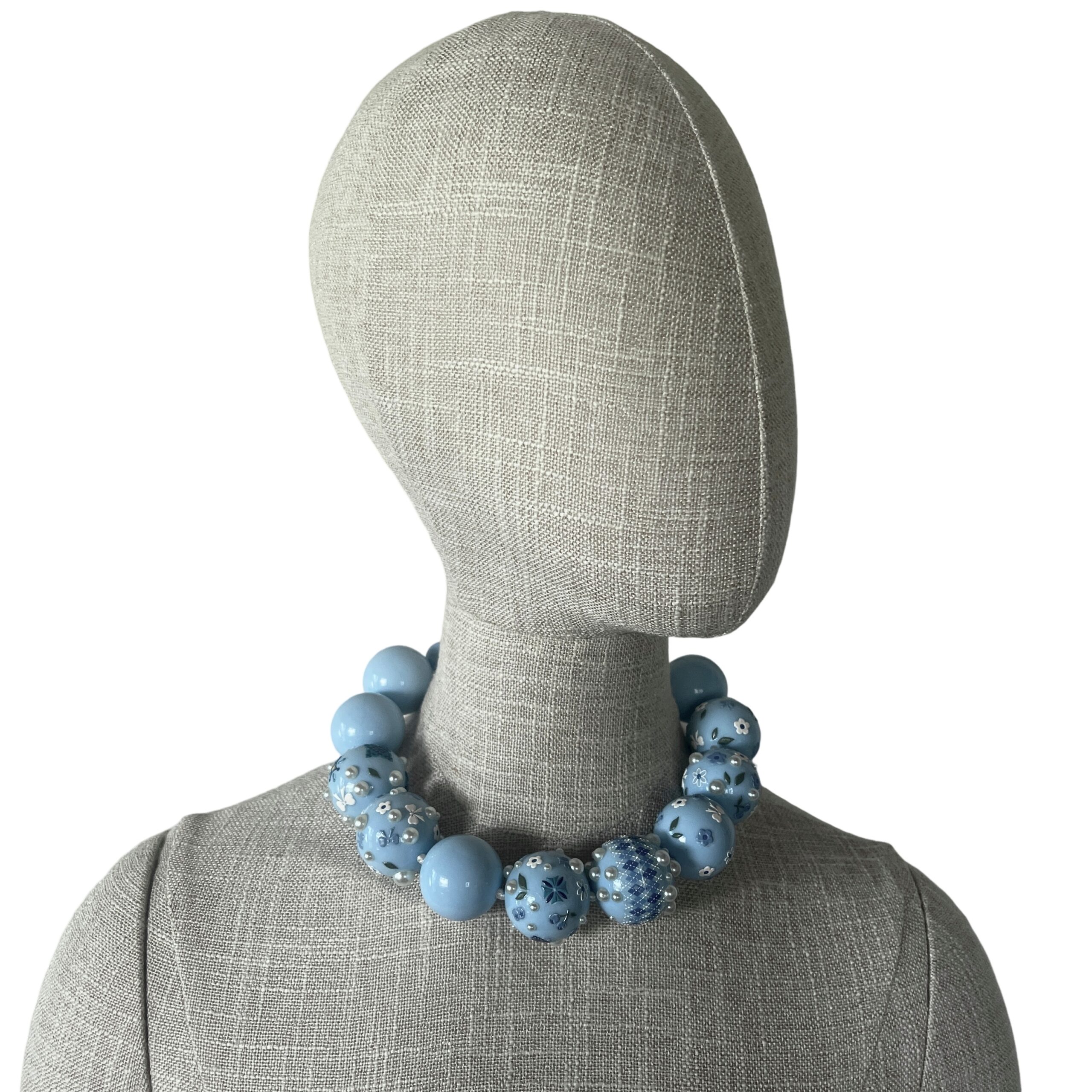 Baby‑blue acrylic bead necklace with floral and bow decorations displayed on a black jewelry bust.