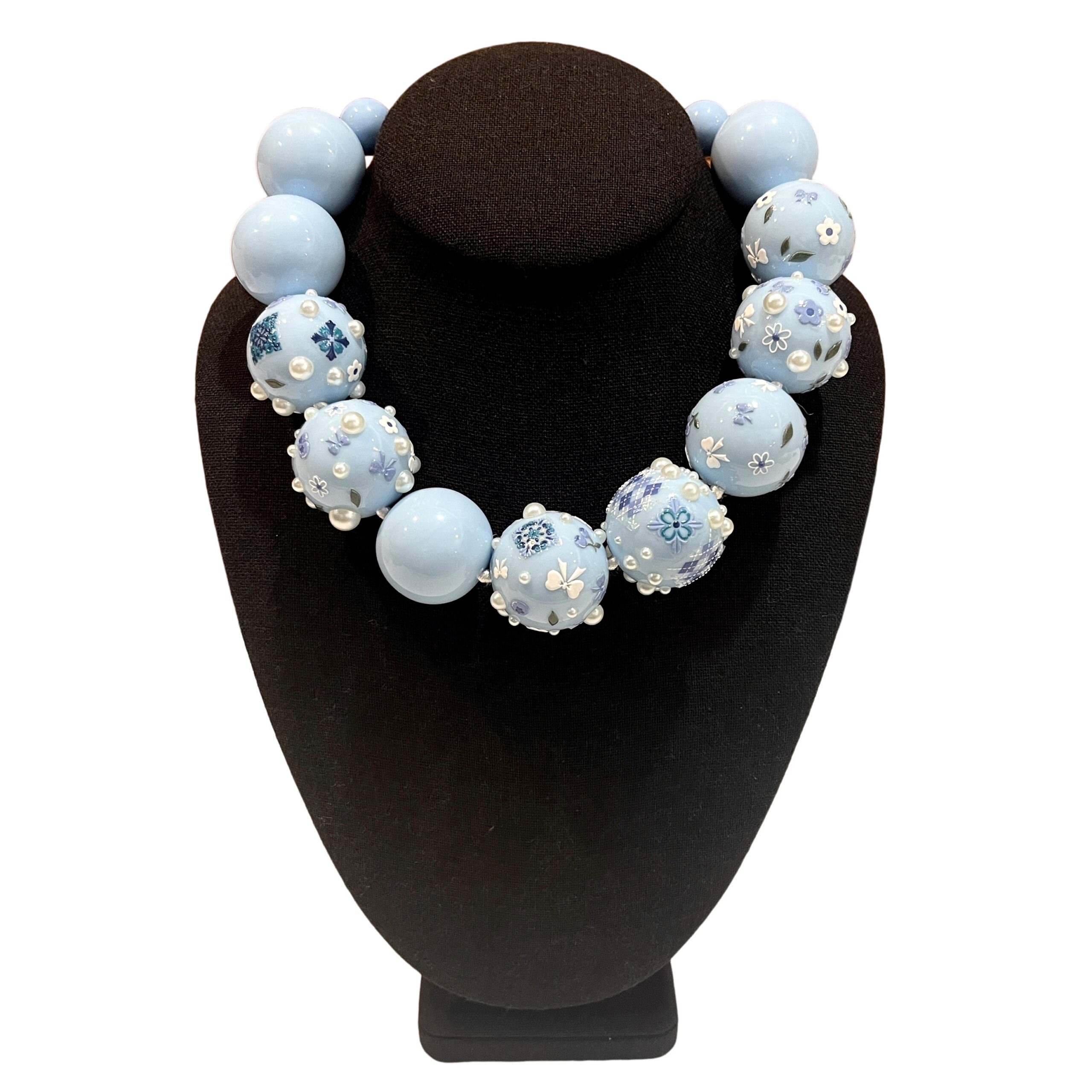 Baby‑blue acrylic bead necklace with floral and bow decorations displayed on a black jewelry bust.